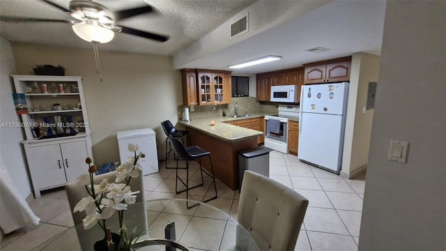 kitchen with a breakfast bar, sink, light tile patterned floors, kitchen peninsula, and white appliances