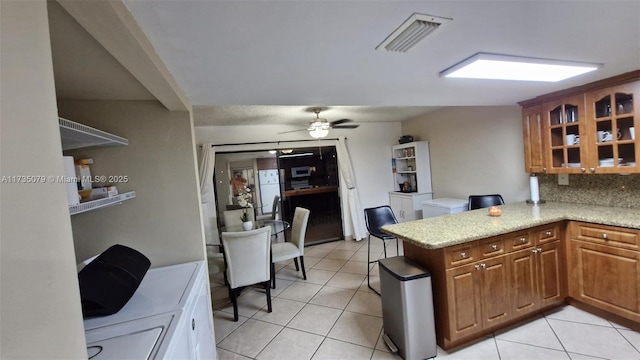 kitchen with light tile patterned floors, kitchen peninsula, ceiling fan, light stone countertops, and backsplash