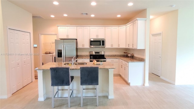 kitchen featuring stainless steel appliances, visible vents, white cabinetry, a sink, and an island with sink