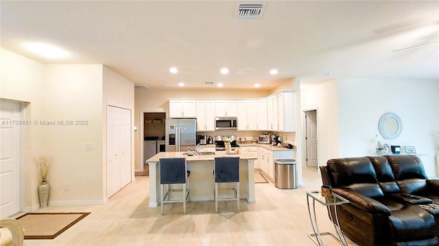 kitchen featuring visible vents, appliances with stainless steel finishes, washing machine and dryer, an island with sink, and a kitchen bar