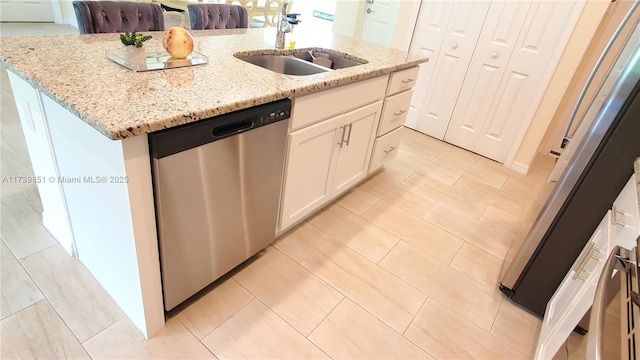 kitchen featuring a sink, white cabinets, light stone countertops, dishwasher, and an island with sink