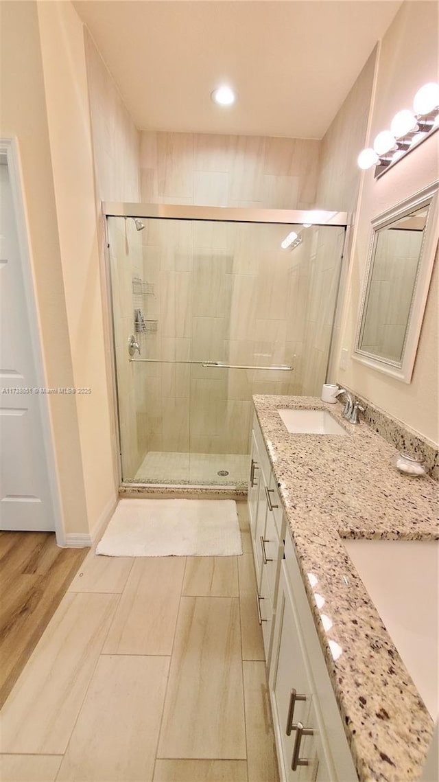 bathroom featuring double vanity, a stall shower, wood tiled floor, and a sink