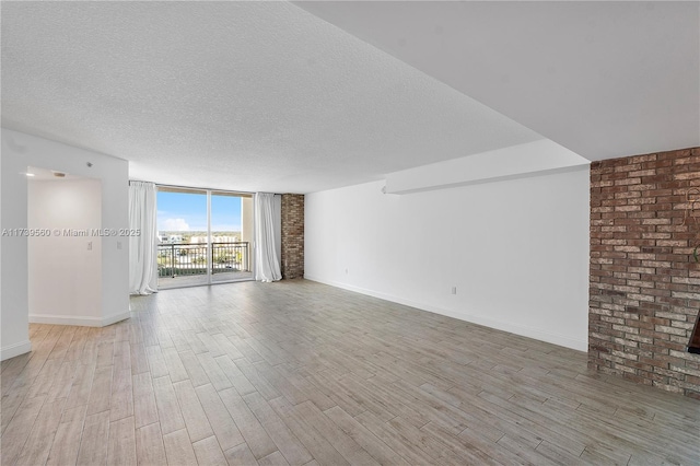 unfurnished living room with a textured ceiling, baseboards, light wood-style flooring, and floor to ceiling windows