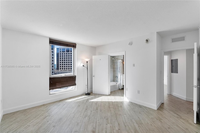 empty room featuring a textured ceiling, visible vents, baseboards, light wood-type flooring, and electric panel