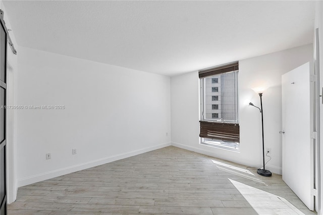 unfurnished room with light wood-type flooring, baseboards, and a textured ceiling