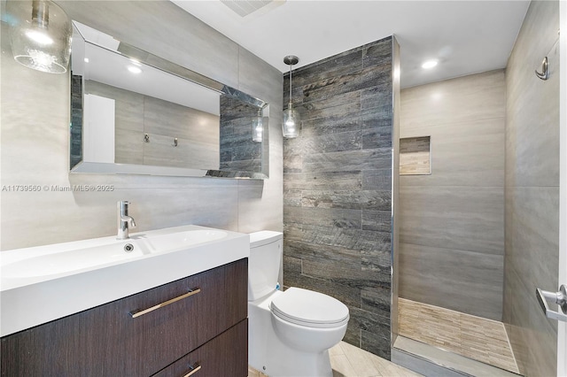 bathroom featuring a walk in shower, toilet, visible vents, vanity, and tile walls