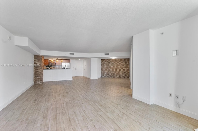 unfurnished living room with visible vents, light wood-style floors, a textured ceiling, brick wall, and baseboards