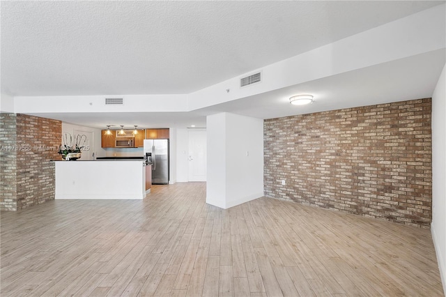 unfurnished living room with visible vents, brick wall, and light wood-style flooring