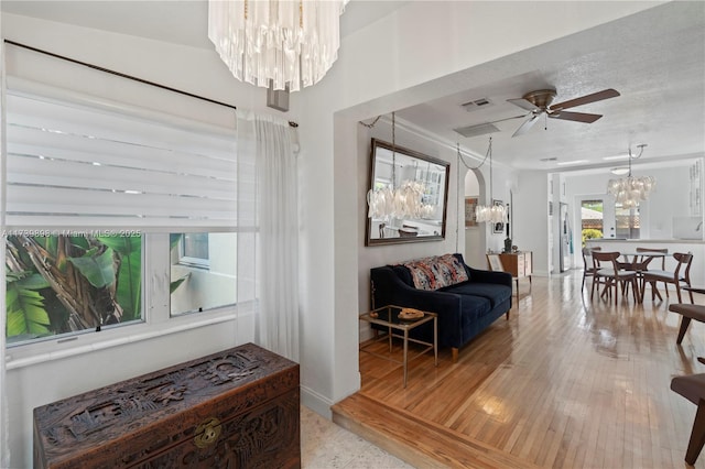 interior space with ceiling fan with notable chandelier, light wood finished floors, a textured ceiling, and visible vents