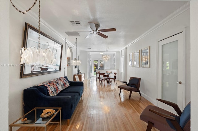 living room featuring baseboards, visible vents, crown molding, light wood-type flooring, and ceiling fan with notable chandelier