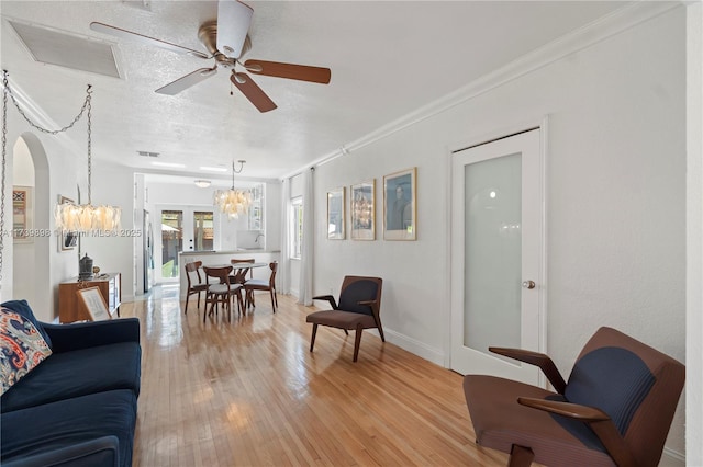 living area featuring baseboards, arched walkways, light wood-style flooring, a textured ceiling, and crown molding