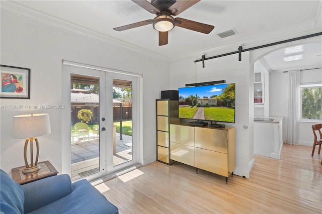 living area with a barn door, visible vents, french doors, light wood-type flooring, and crown molding