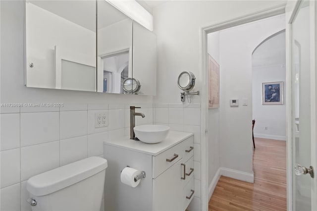 bathroom featuring tile walls, decorative backsplash, toilet, vanity, and wood finished floors