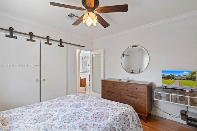 bedroom featuring a barn door, visible vents, ceiling fan, ornamental molding, and wood finished floors