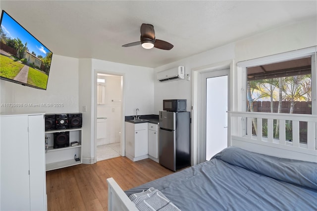 bedroom with ensuite bathroom, wood finished floors, a sink, freestanding refrigerator, and a wall mounted air conditioner