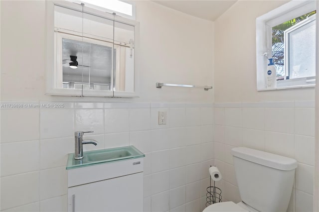 bathroom with tile walls, a wainscoted wall, vanity, and toilet