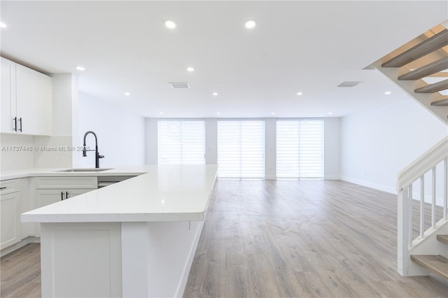 kitchen with white cabinetry, sink, light hardwood / wood-style floors, and a healthy amount of sunlight