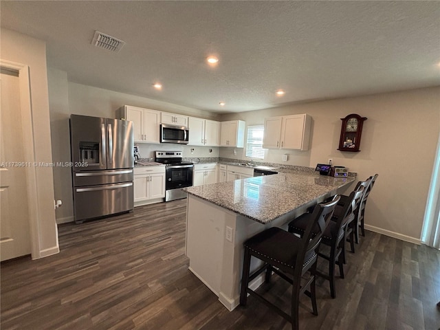 kitchen featuring white cabinetry, a kitchen bar, kitchen peninsula, and appliances with stainless steel finishes