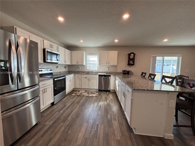 kitchen with sink, a breakfast bar area, dark stone countertops, stainless steel appliances, and white cabinets