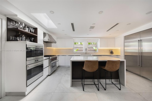 kitchen featuring sink, high end appliances, a kitchen island, white cabinets, and wall chimney range hood