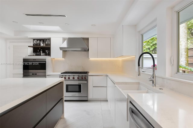 kitchen with appliances with stainless steel finishes, tasteful backsplash, white cabinetry, sink, and wall chimney exhaust hood