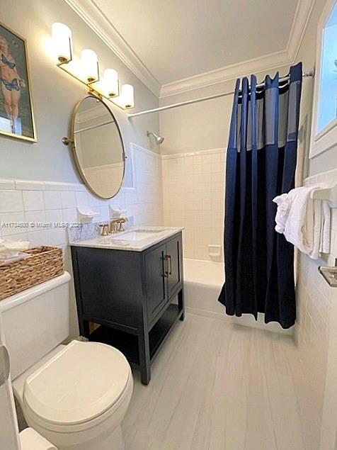 full bathroom featuring shower / tub combo with curtain, tile walls, vanity, toilet, and crown molding