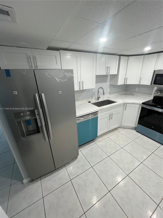 kitchen featuring a drop ceiling, sink, stainless steel appliances, and white cabinets