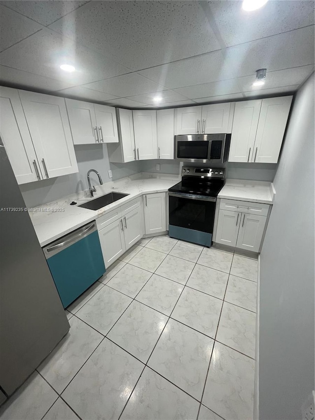 kitchen with sink, a paneled ceiling, light tile patterned floors, stainless steel appliances, and white cabinets