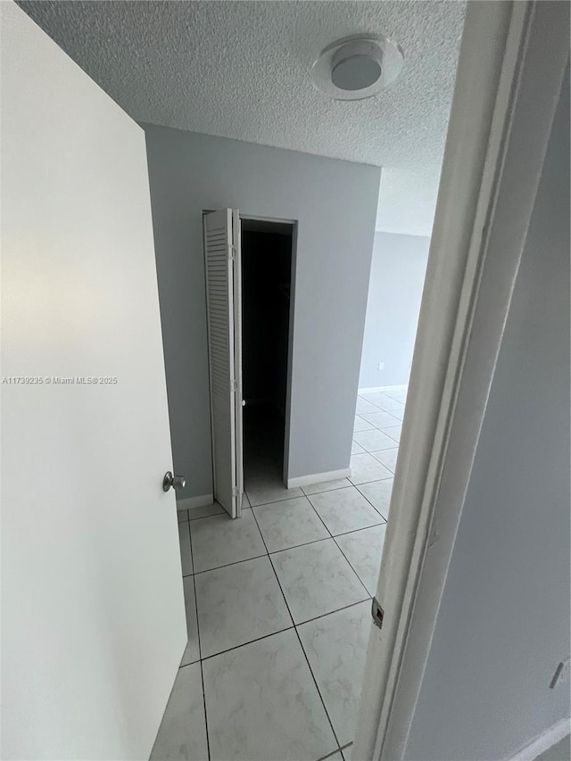 hallway with a textured ceiling and light tile patterned flooring