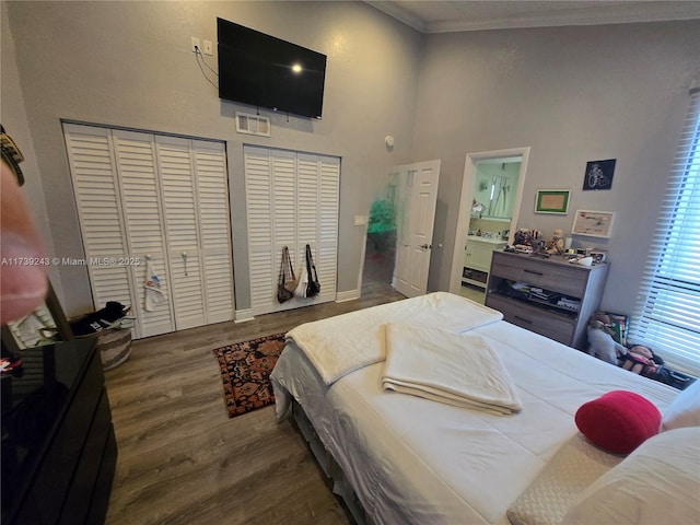 bedroom with dark hardwood / wood-style flooring, connected bathroom, crown molding, and a towering ceiling