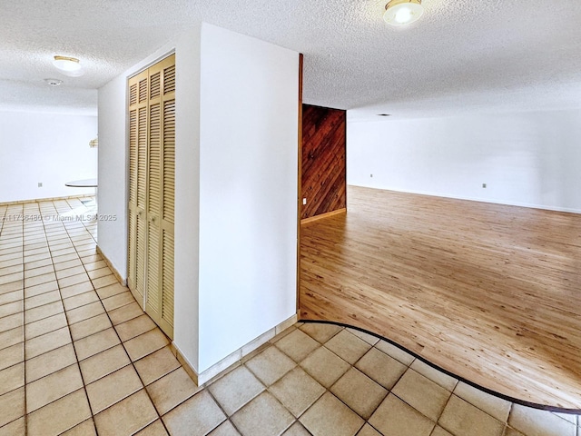 hallway featuring wooden walls, light hardwood / wood-style flooring, and a textured ceiling