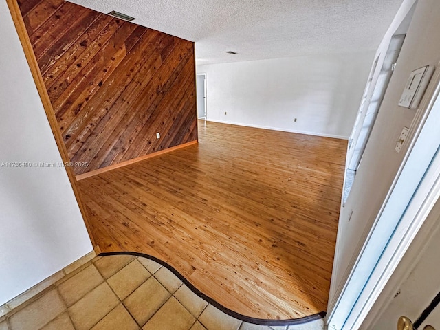 unfurnished room featuring hardwood / wood-style flooring, a textured ceiling, and wood walls