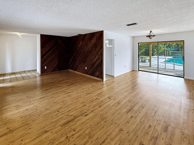 unfurnished living room featuring hardwood / wood-style floors, wooden walls, and a textured ceiling