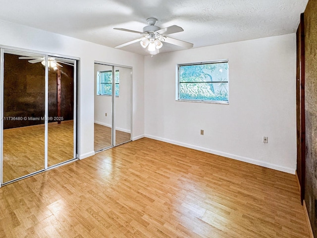 unfurnished bedroom with ceiling fan, two closets, hardwood / wood-style floors, and a textured ceiling