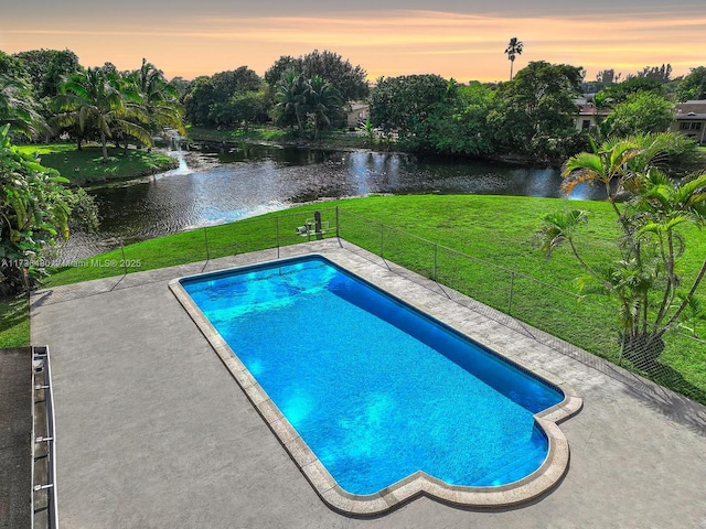 pool at dusk with a patio area, a lawn, and a water view