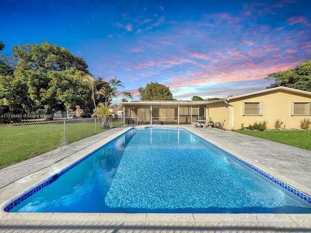 pool at dusk with a sunroom and a lawn