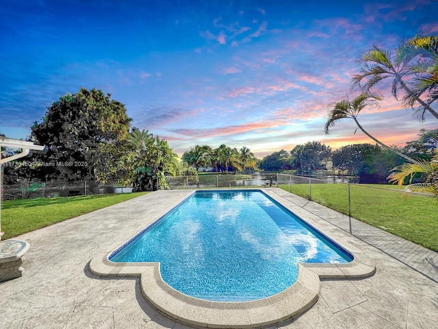 pool at dusk with a patio and a lawn