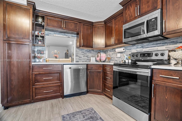 kitchen with appliances with stainless steel finishes, dark brown cabinets, a textured ceiling, decorative backsplash, and light wood-type flooring