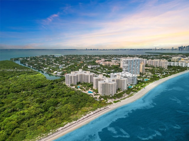 aerial view at dusk featuring a water view and a beach view