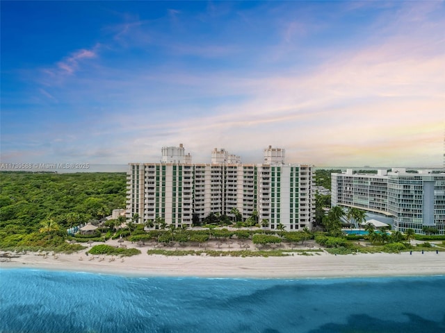 aerial view at dusk featuring a view of the beach and a water view