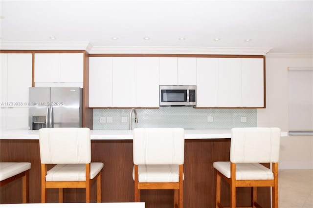 kitchen featuring stainless steel appliances, a breakfast bar, white cabinets, and backsplash