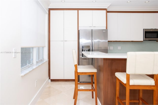 kitchen with stainless steel appliances, ornamental molding, white cabinets, and a kitchen breakfast bar