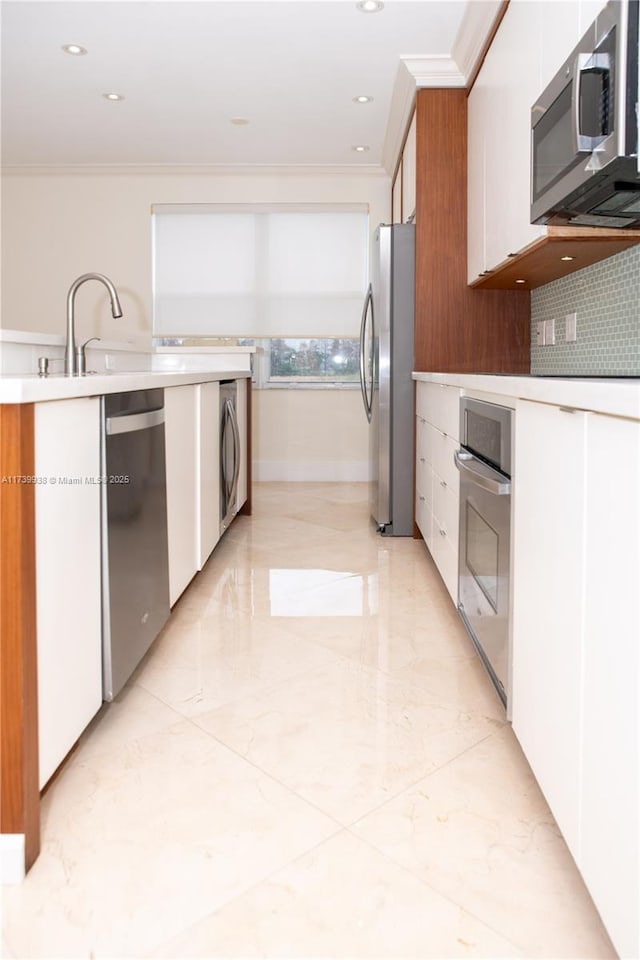 kitchen with white cabinetry, crown molding, stainless steel appliances, washer / clothes dryer, and decorative backsplash