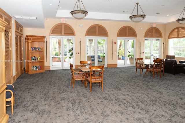 carpeted dining space featuring a towering ceiling, a tray ceiling, and french doors