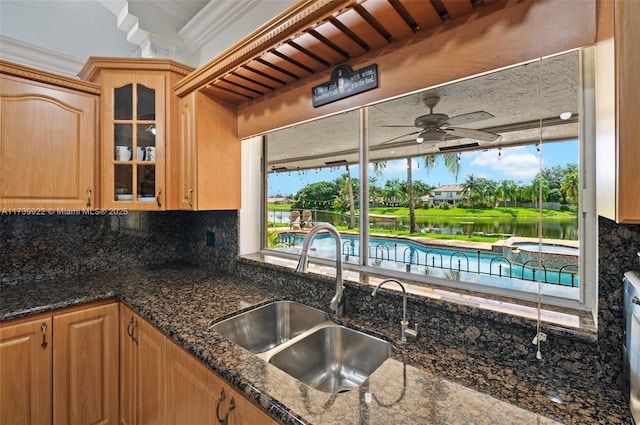 kitchen with ornamental molding, sink, dark stone countertops, and backsplash