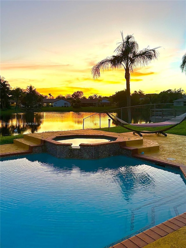 pool at dusk with a water view and an in ground hot tub