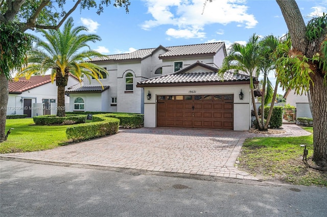 mediterranean / spanish house with stucco siding, a tile roof, an attached garage, decorative driveway, and a front yard