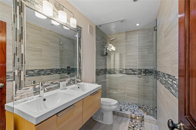 bathroom with tile walls, backsplash, vanity, a shower with shower door, and toilet