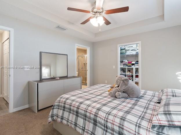 bedroom with ceiling fan, a tray ceiling, light carpet, a walk in closet, and a closet