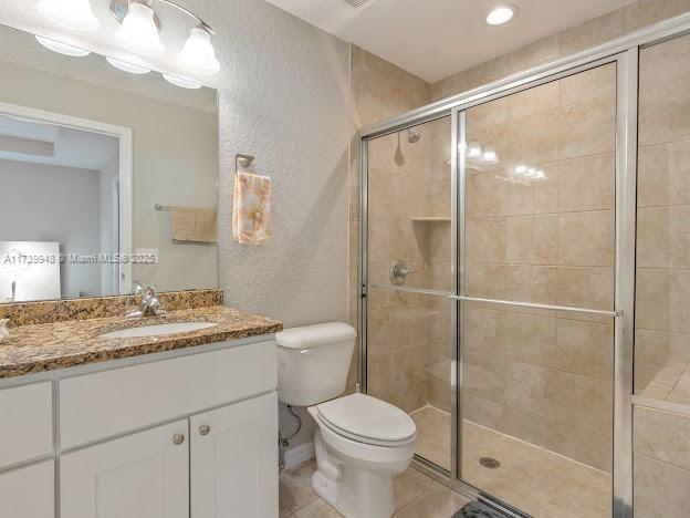 bathroom featuring vanity, toilet, tile patterned flooring, and a shower with door